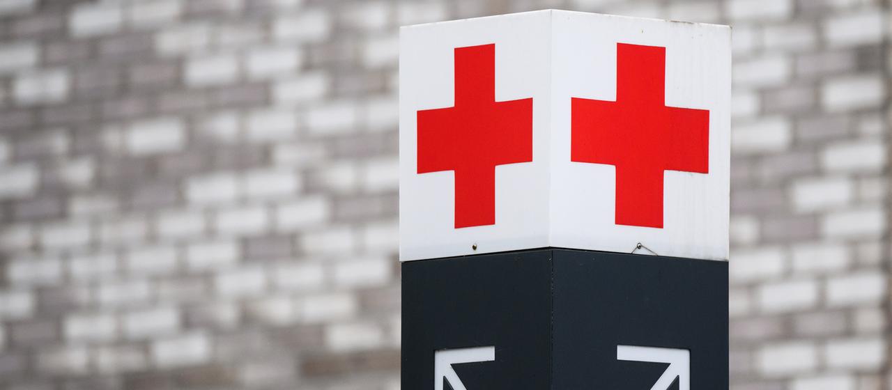 Ein Schild mit einem roten Kreuz weist den Weg zur Notaufnahme.