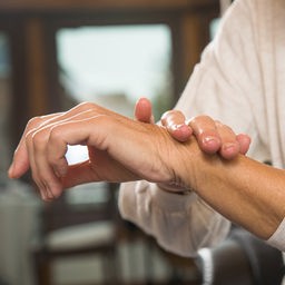 Eine ältere Frau fasst sich ans Handgelenk.