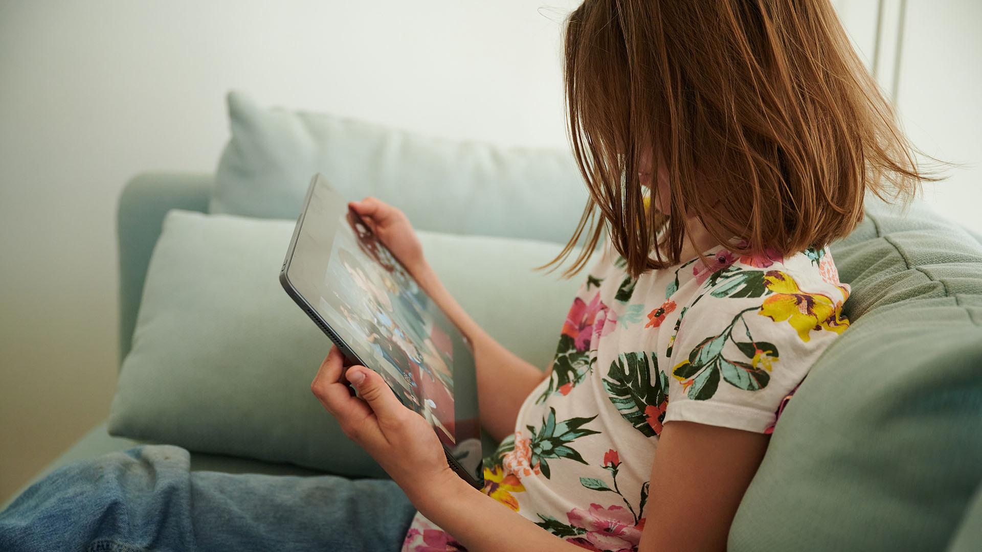Ein Mädchen sitzt auf dem Sofa und guckt in ihr Tablet. | picture alliance/dpa