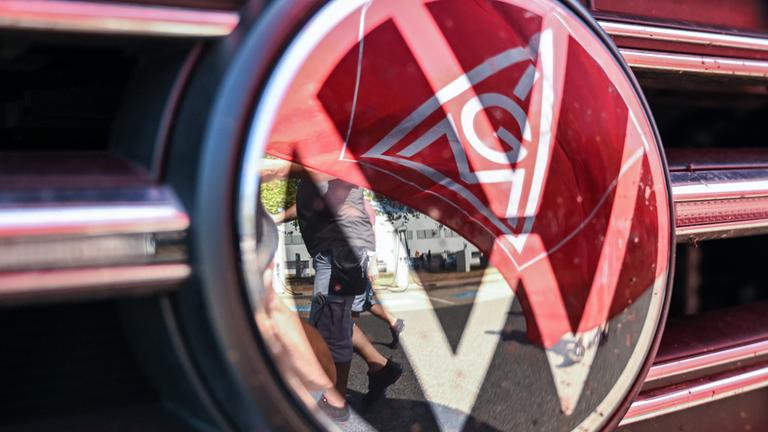 Eine Fahne der IG Metall spiegelt sich in einem VW Logo.