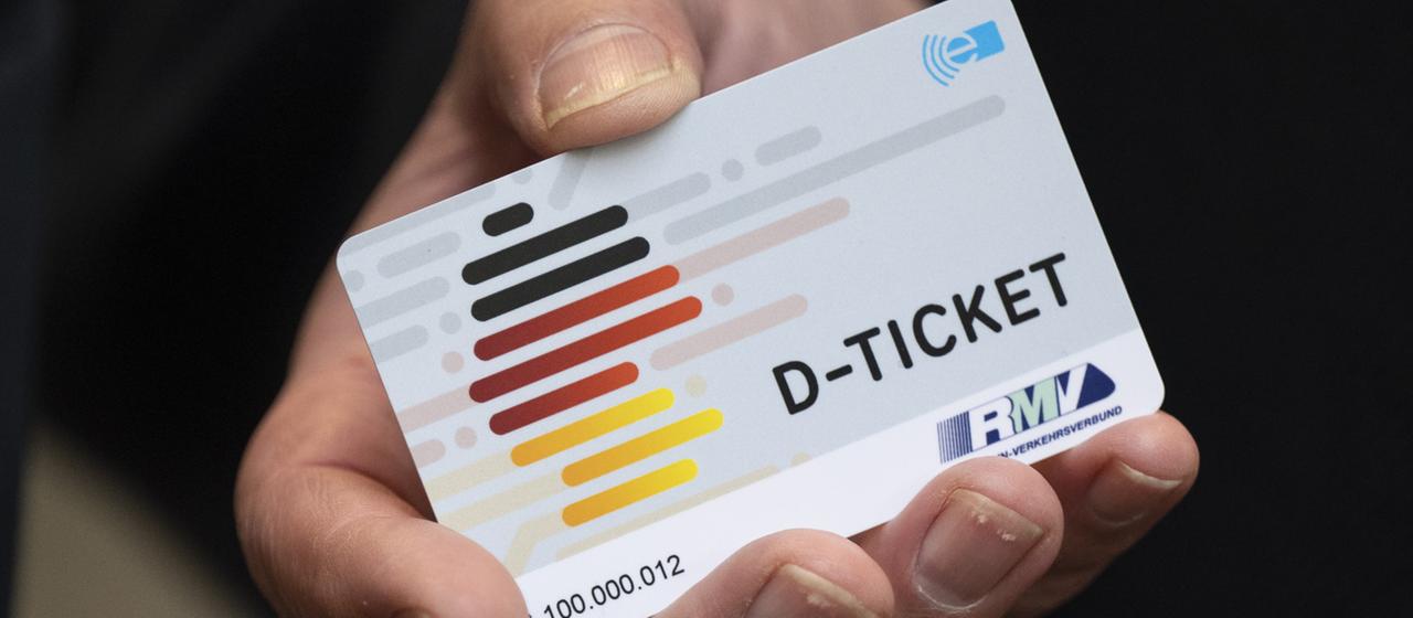 Eine Hand hält ein Deutschlandticket.