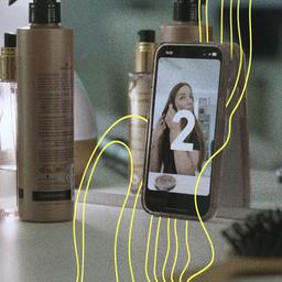 Ein Handy ist vor einem Spiegel Aufgestellt - die Kamera ist an. Vor dem Handy macht sich ein Mädchen bereit für eine Video-Aufzeichnung.