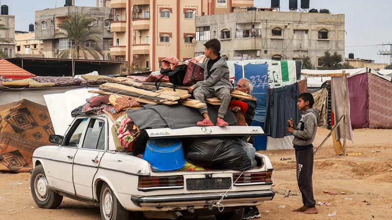 Ein Kind sitzt auf Gegenständen, die mit Seilen auf einem Auto befestigt sind.