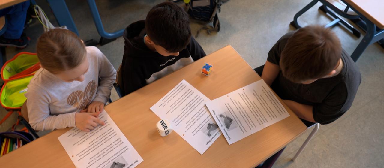 Eine Schülerin und zwei Schüler lesen.