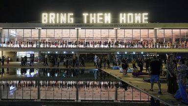 Menschen stehen unter einer Leuchtschrift mit dem Text "Bring Them Home" ("Bringt sie nach Hause"), bei einer Demonstration, die die Rückkehr der Geiseln fordert.