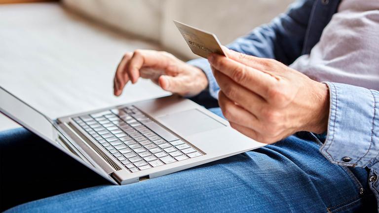 Ein Mann sitzt mit einer Kreditkarte an einem Laptop und gibt Daten ein.