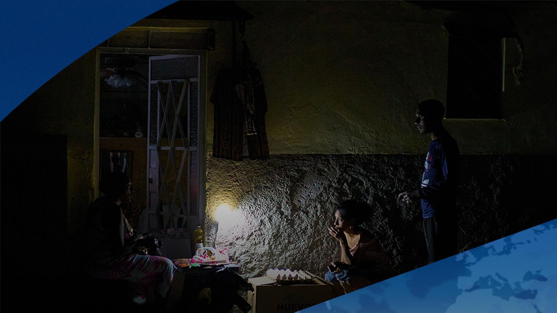 Menschen sitzen in Kuba vor einem Haus. Ein Licht steht auf einem Tisch, der Rest, dunkel. | AP