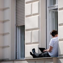 Ein Mann arbeitet auf dem Fensterbrett seiner Wohnung am Computer