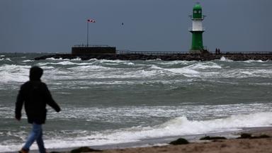 Ein Spaziergänger am Strand von Warnemünde, das Wasser der aufgepeitschten Ostsee wird an den Strand gedrückt.