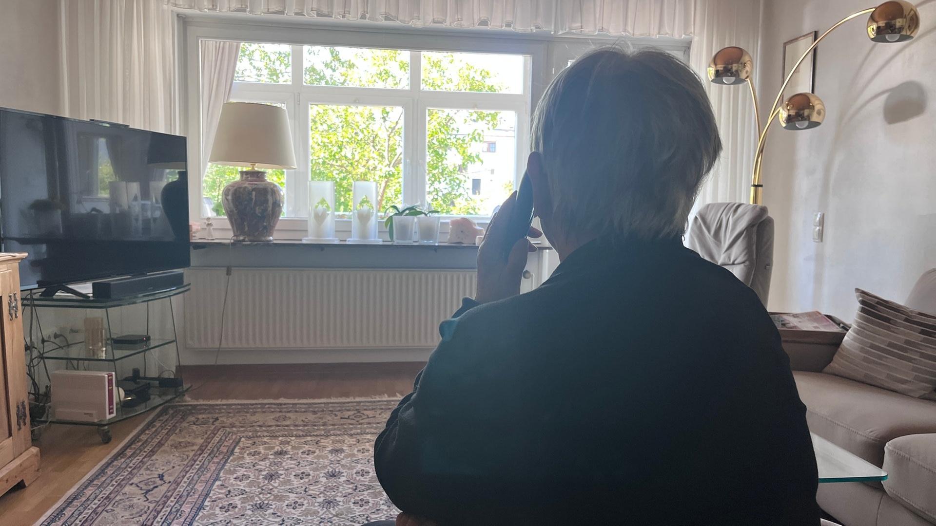 Eine Frau sitzt in einem Wohnzimmer und hat ein Telefon am Ohr | SWR