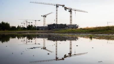 Spiegelung in einer Pfütze von Kränen und Baustellen einer Neubausiedlung.