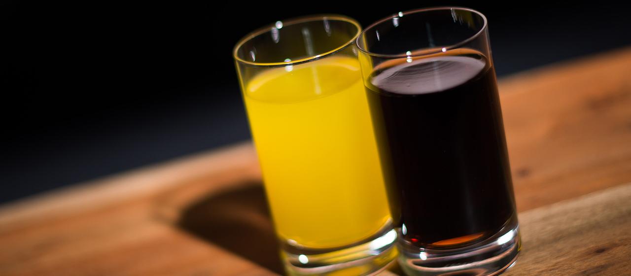 Ein Glas mit Cola steht neben einem Glas mit Orangenlimonade.