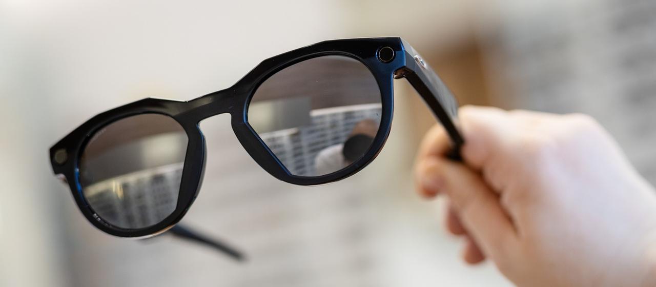 Eine Frau hält in einem Brillenfachgeschäft eine smarte Datenbrille der Firma Oakley Meta in ihrer Hand.