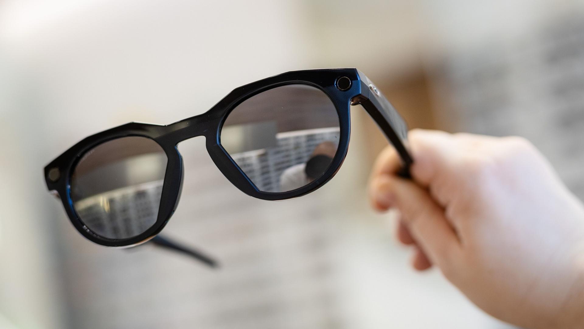 Eine Frau hält in einem Brillenfachgeschäft eine smarte Datenbrille der Firma Oakley Meta in ihrer Hand. | Christoph Schmidt/dpa