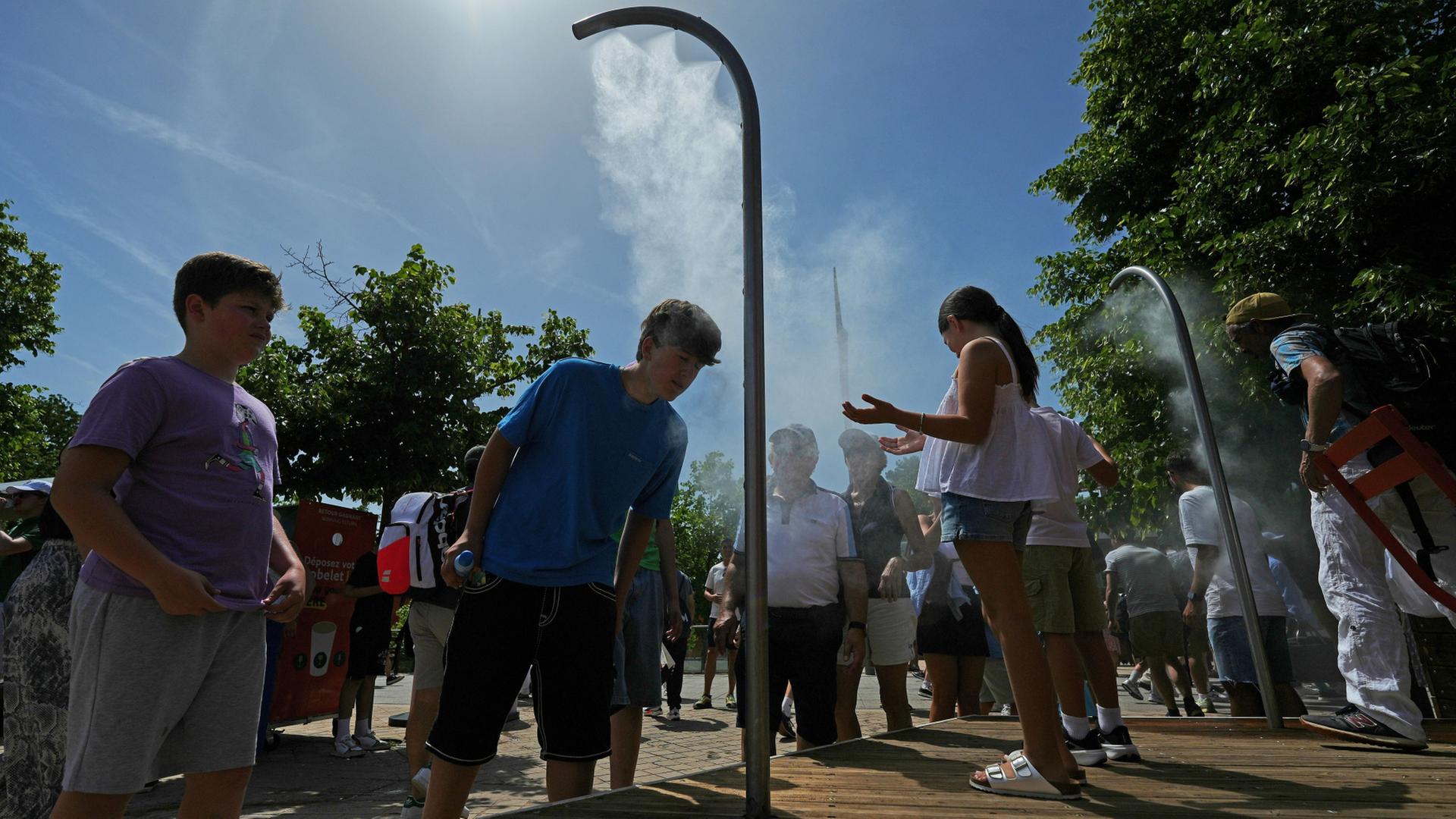 Menschen kühlen sich mit Wasser aus Sprinklern ab | Aurelien Morissard/AP/dpa
