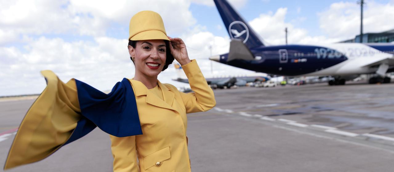 Eine Hostess trägt eine frühere Lufthansa-Uniform vor einem Passagierflugzeug der Lufthansa auf dem Flughafen Berlin-Brandenburg (BER) bei der Feier zum 100. Jahrestag des Erstflugs.