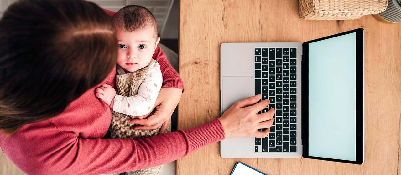Frau mit Baby sitzt vor einem Laptop.