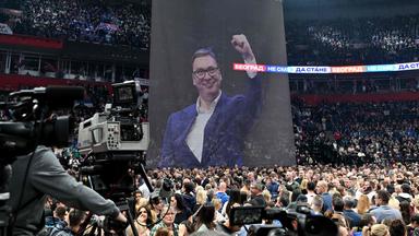 Unterstützer von Serbiens Präsidenten Vucic versammeln sich vor einem großen Plakat mit dem Konterfei des Präsidenten in Belgrad.