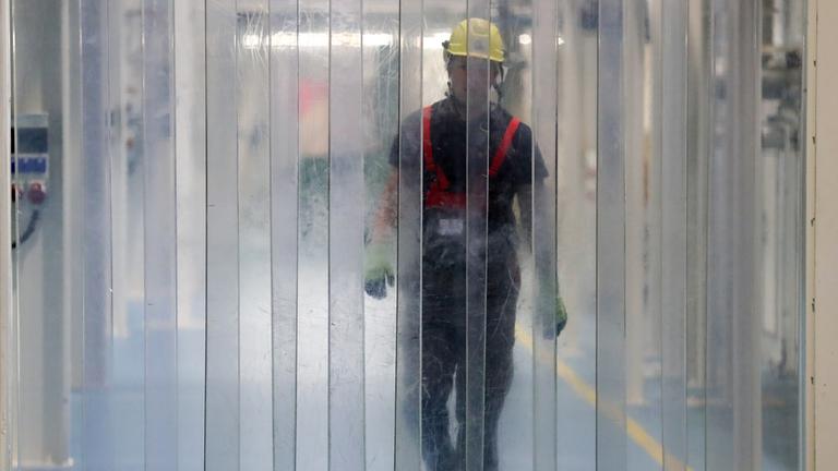 Ein Mitarbeiter eines Chemie-Unternehmens im Chemiepark Leuna geht auf einen Streifenvorhang aus Kunststoff zu.