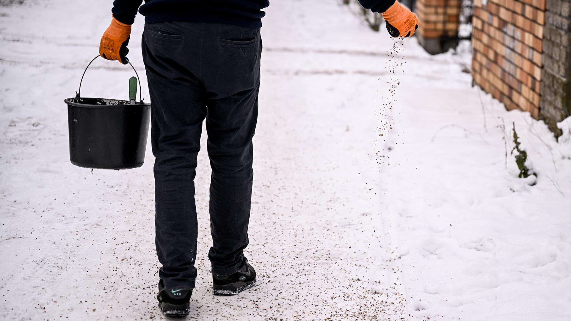 Ein Mann streut den Gehsteig vor seinem Haus.  | dpa
