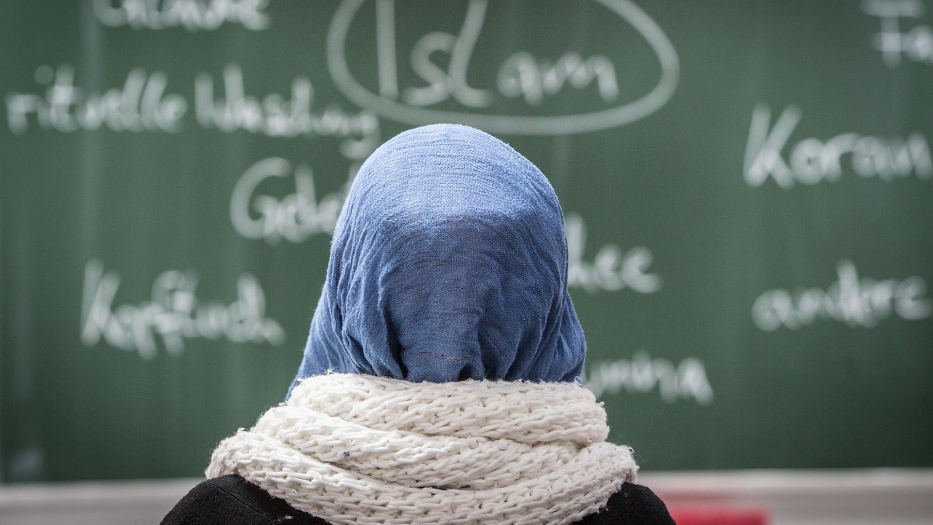 Eine Schülerin mit Kopftuch sitzt vor einer Tafel. | dpa