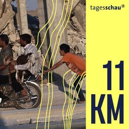 Syrer tragen zwei Ziegen auf einem Motorrad vor zerstörten Gebäuden südlich von Kobane, Syrien.