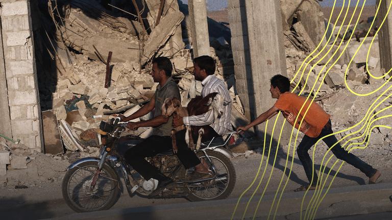 Syrer tragen zwei Ziegen auf einem Motorrad vor zerstörten Gebäuden südlich von Kobane, Syrien.