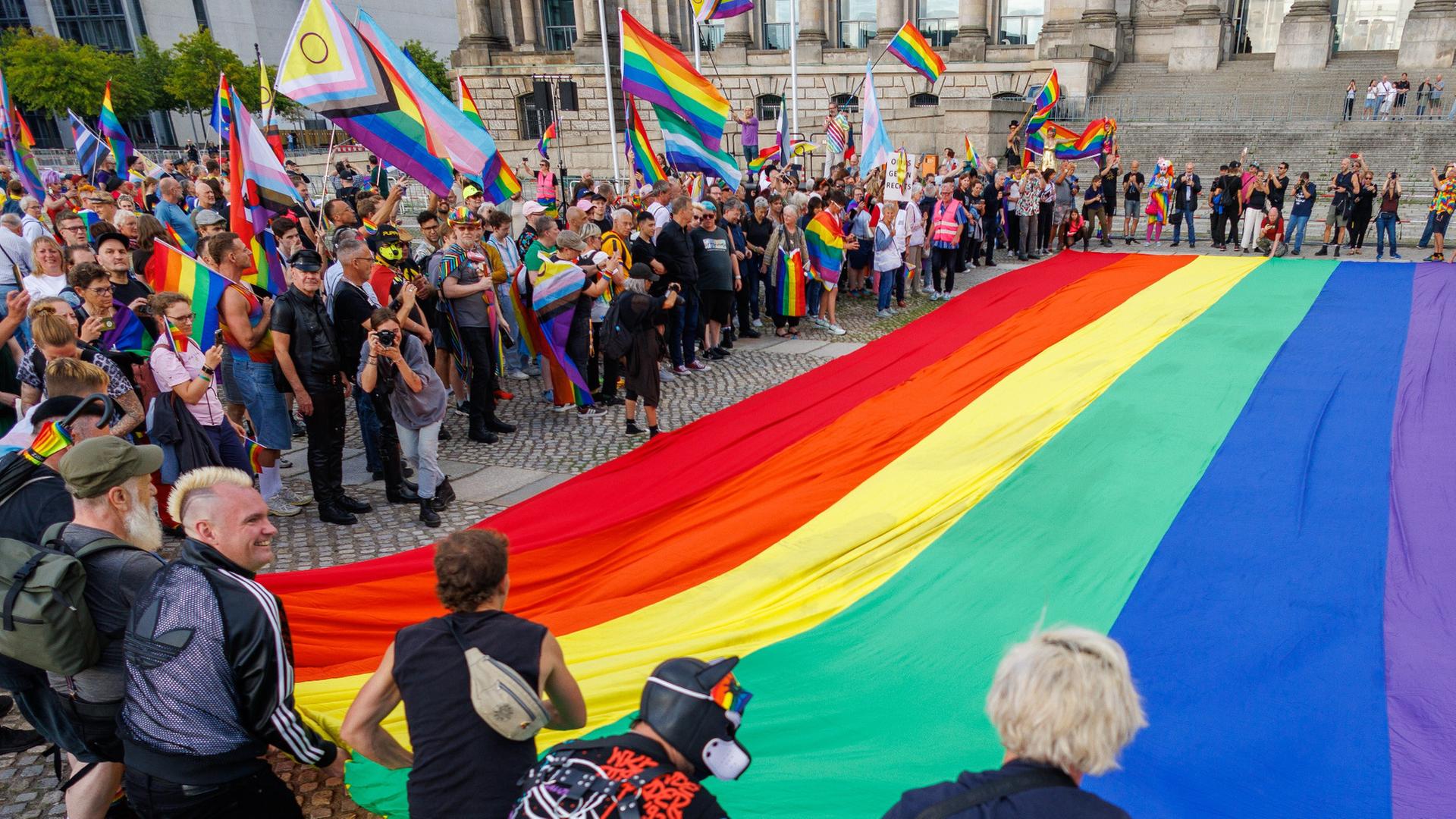 Teilnehmer einer Protestaktion rollen eine 400 Quadratmeter große Regenbogenflagge vor dem Bundestag aus als Protest gegen Handlungen der Bundesregierung (Quelle: picture alliance/dpa/Carsten Koall). | dpa/Carsten Koall