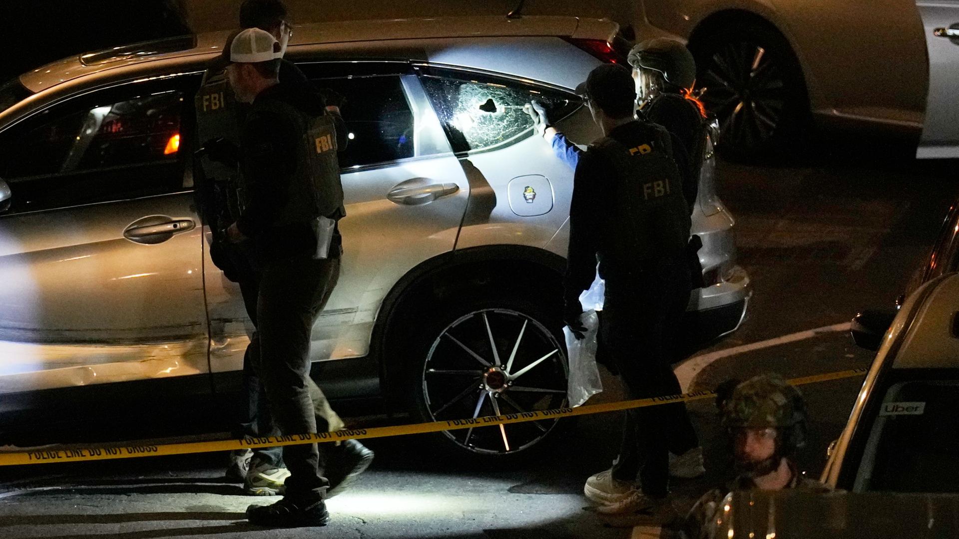 FBI-Agenten untersuchen ein Auto, in der hinteren Scheibe ist ein Einschussloch. | Seth Wenig/AP/dpa
