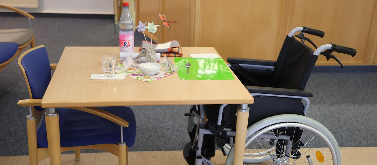 A wheelchair sits at a dining table in a nursing home.
