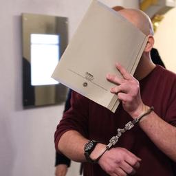 Ein Angeklagter hält sich eine Mappe vor das Gesicht