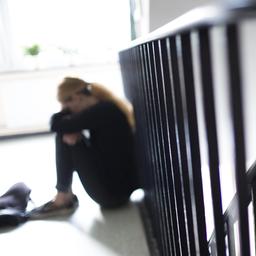 Eine Frau sitzt an ein Treppengeländer gelehnt und hat den Kopf und die Arme auf die Knie gelegt.