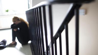 Eine Frau sitzt an ein Treppengeländer gelehnt und hat den Kopf und die Arme auf die Knie gelegt.