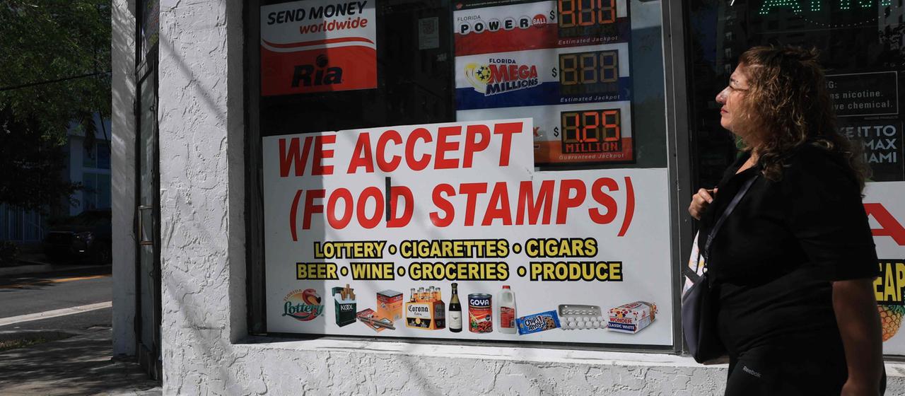 Ein Schild mit der Aufschrift "We accept (Food Stamps)" hängt an einem Ladenfenster