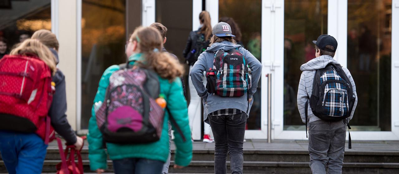 Schülerinnen und Schüler gehen zum Eingang eines Gymnasiums.