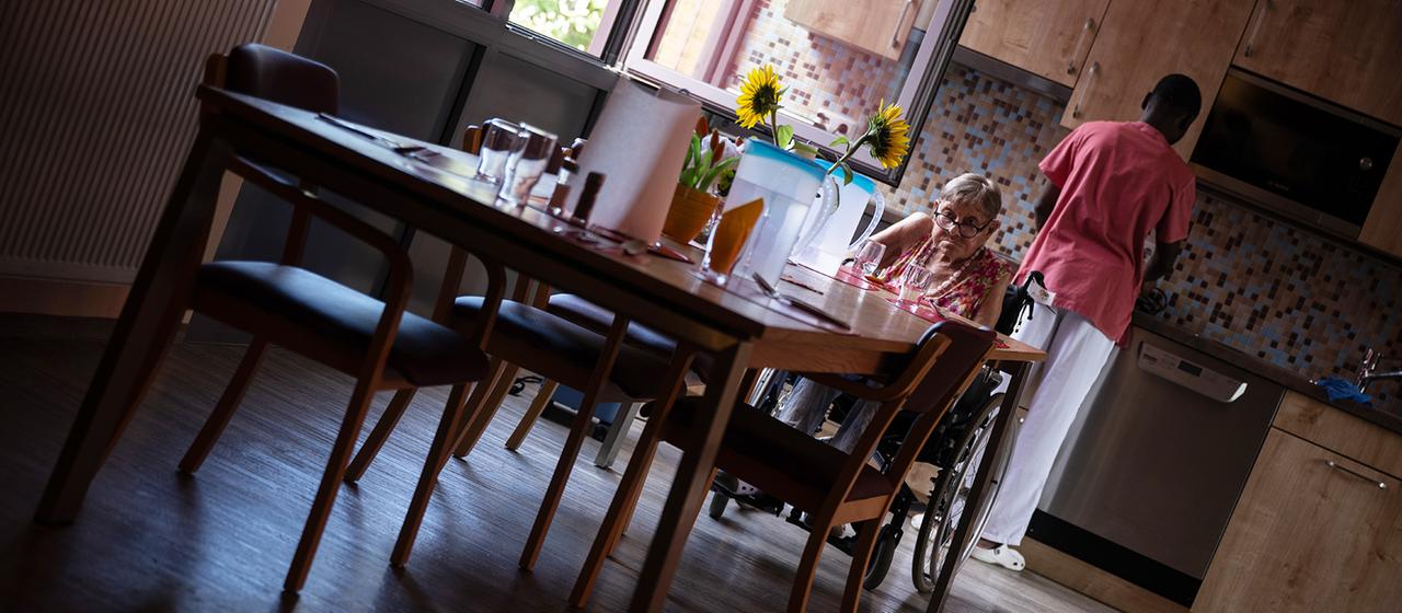 Eine Bewohnerin sitzt in einer Pflegeeinrichtung an einem Tisch.
