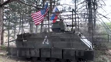 Ein Panzer mit den Flaggen der USA und Russlands steht im Wald (Screenshot von Russia Today).