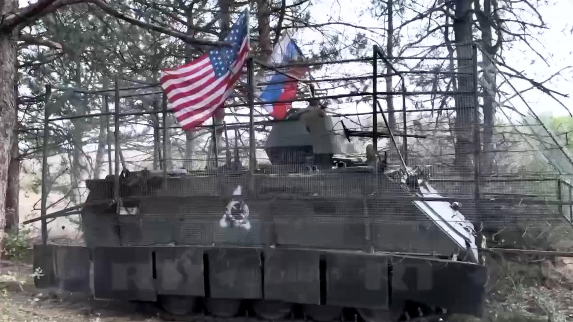 Ein Panzer mit den Flaggen der USA und Russlands steht im Wald (Screenshot von Russia Today). | Russia Today