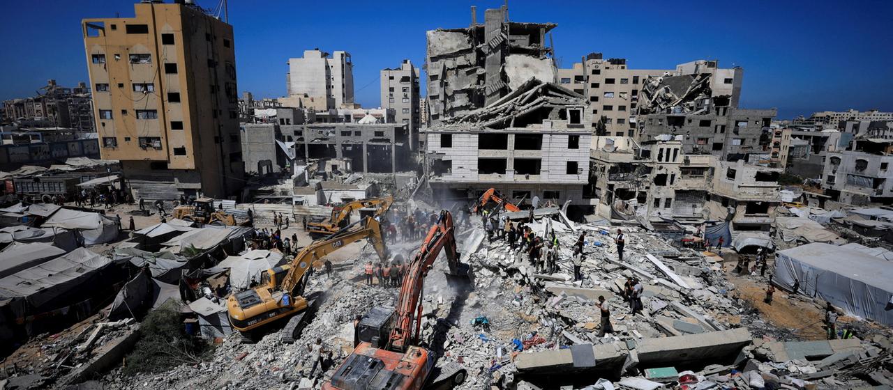 Bagger und Hilfskräfte arbeiten an einem eingestürzten Wohngebäude in Gaza-Stadt.