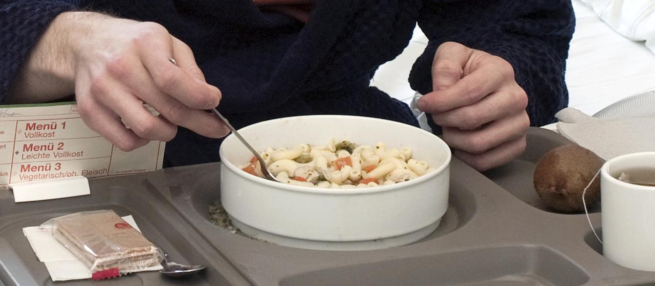 Ein Patient sitzt vor einem Tablett mit Essen in einem Krankenhaus.