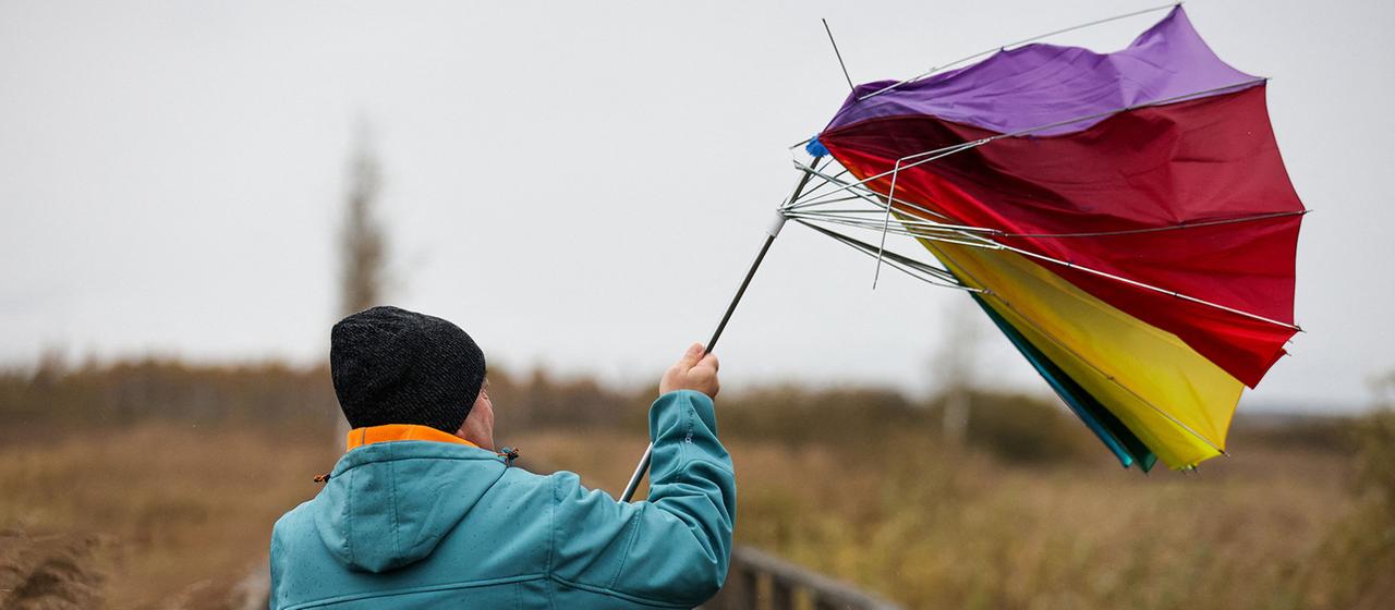 Ein Mann hält auf dem Steg am Federsee seinen Regenschirm fest, der von einer Sturmböe erfasst wird.