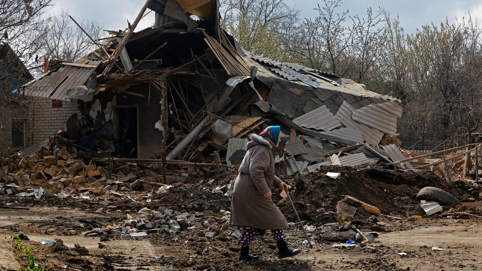 Eine ältere Frau geht vor einem zerstörten Gebäude entlang. | REUTERS