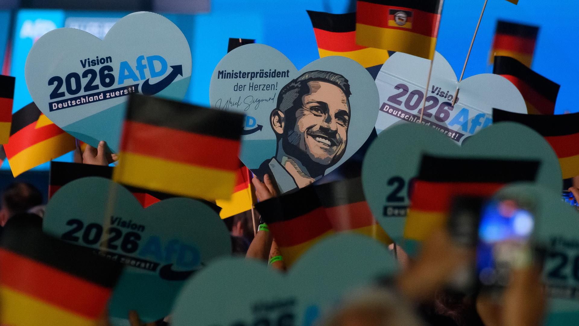 Menschen schwenken Deutschlandfahnen und halten Herzen mit dem Porträt von Ulrich Siegmund hoch. | Klaus-Dietmar Gabbert/dpa