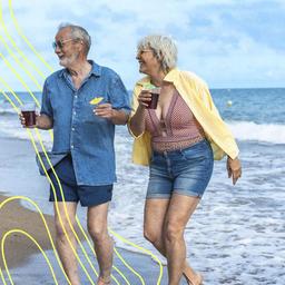 Gruppe glücklicher älterer Freunde, die lachen und barfuß am Sandstrand spazieren gehen.