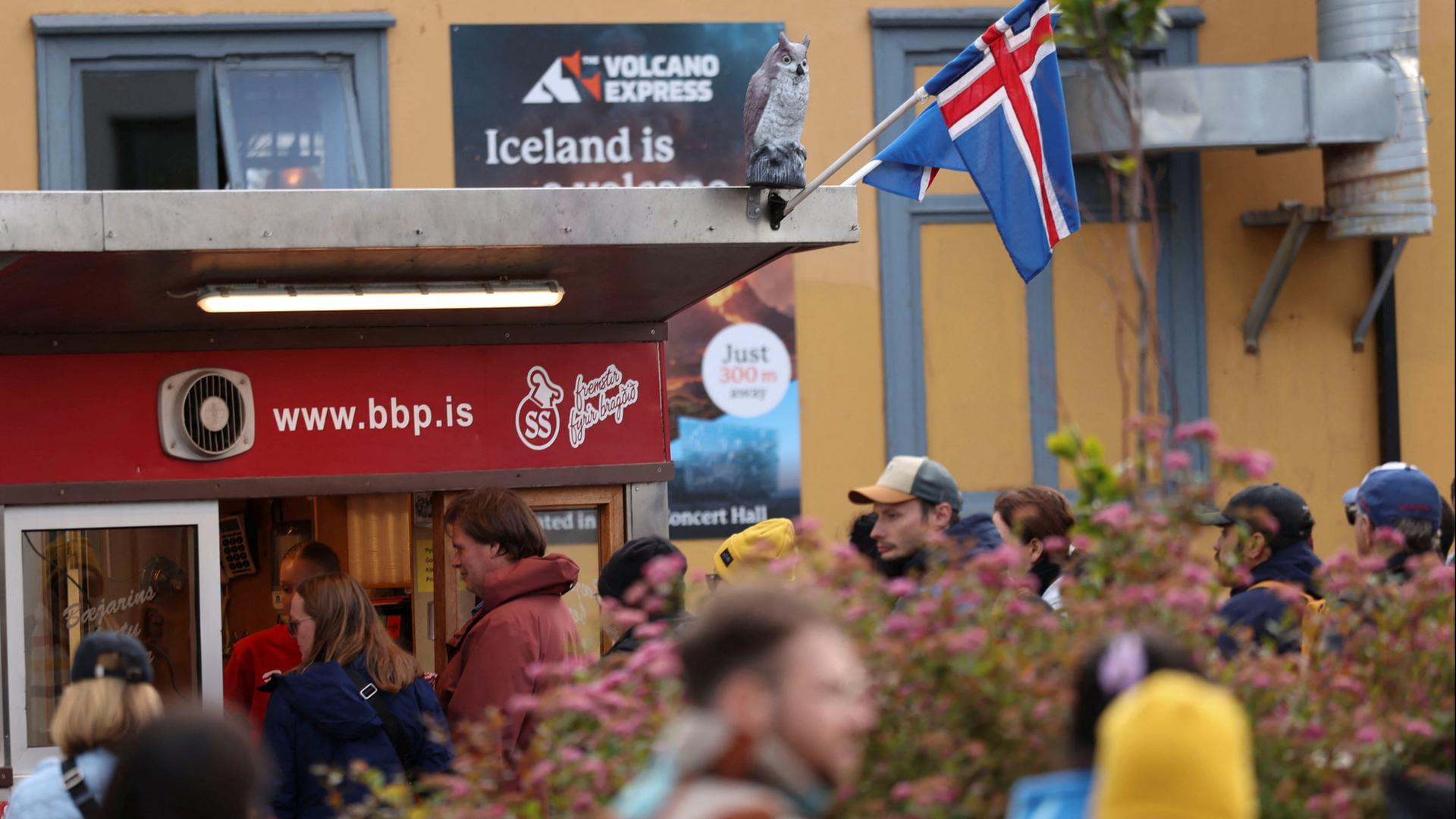 Touristen sind vor einem HotDog-Laden in Reykjavik zu sehen, an dem eine Island-Flagge weht | REUTERS