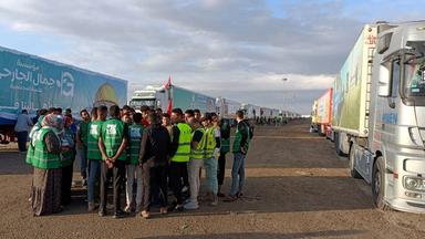 Eine Menschengruppe wartet neben einem Lastwagenkonvoi am Grenzübergang Rafah