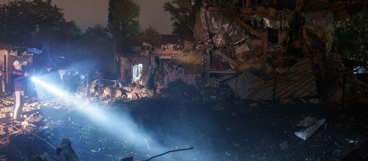 Ein Mann scheint mit einer Taschenlampe auf ein Haus in Kiew, das von einer Drohne zerstört wurde.