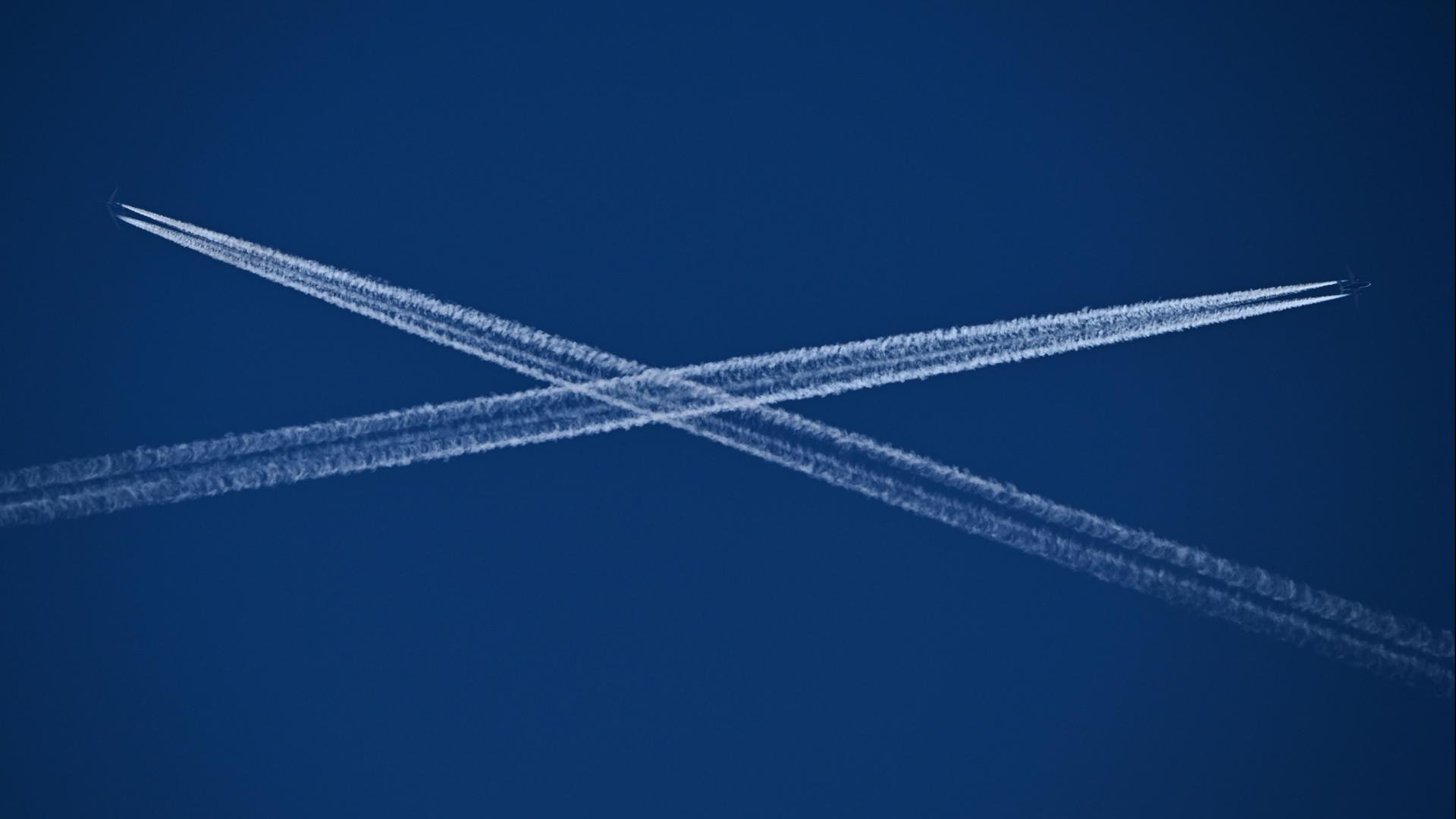 Die Routen zweier Passagiermaschinen, die Kondensstreifen hinter sich herziehen, kreuzen sich am blauen Himmel Ã¼ber Frankfurt. | Arne Dedert/dpa