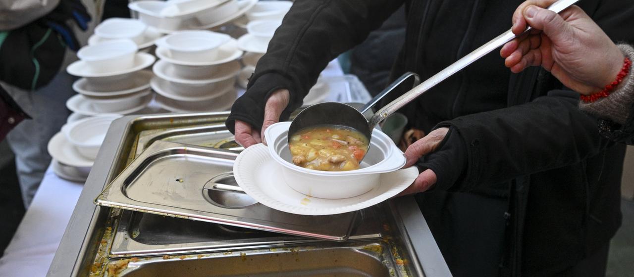Eine Helferin gibt für wohnungslose Menschen heiße Suppe aus.