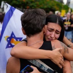 Zwei Menschen umarmen sich vor einer Israel-Flagge.